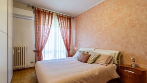 Ein Schlafzimmer mit Bett, Vorhängen, Heizkörper, Holzboden und Nachttisch.