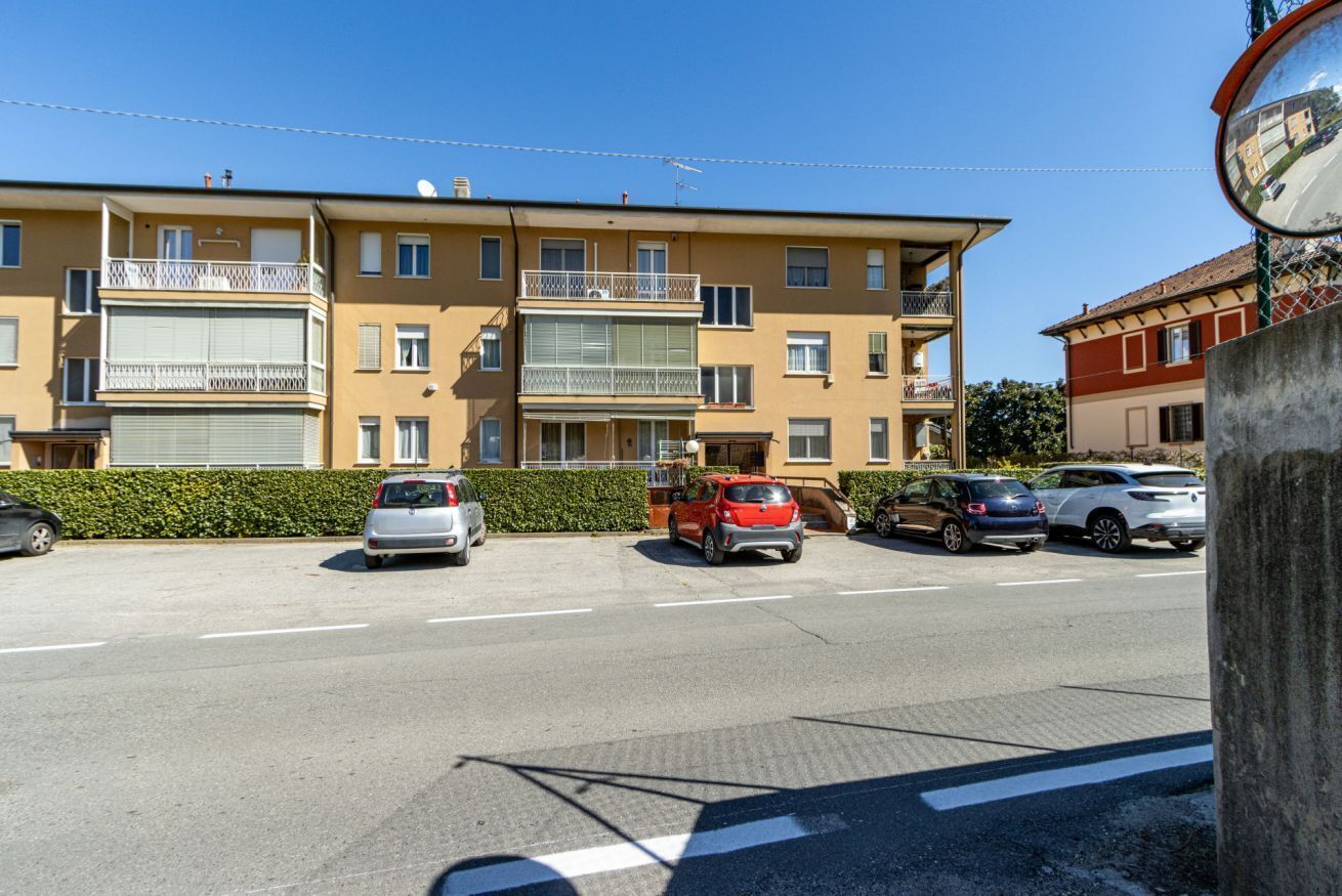 Un edificio residenziale a più piani con balconi, auto parcheggiate e cielo sereno.