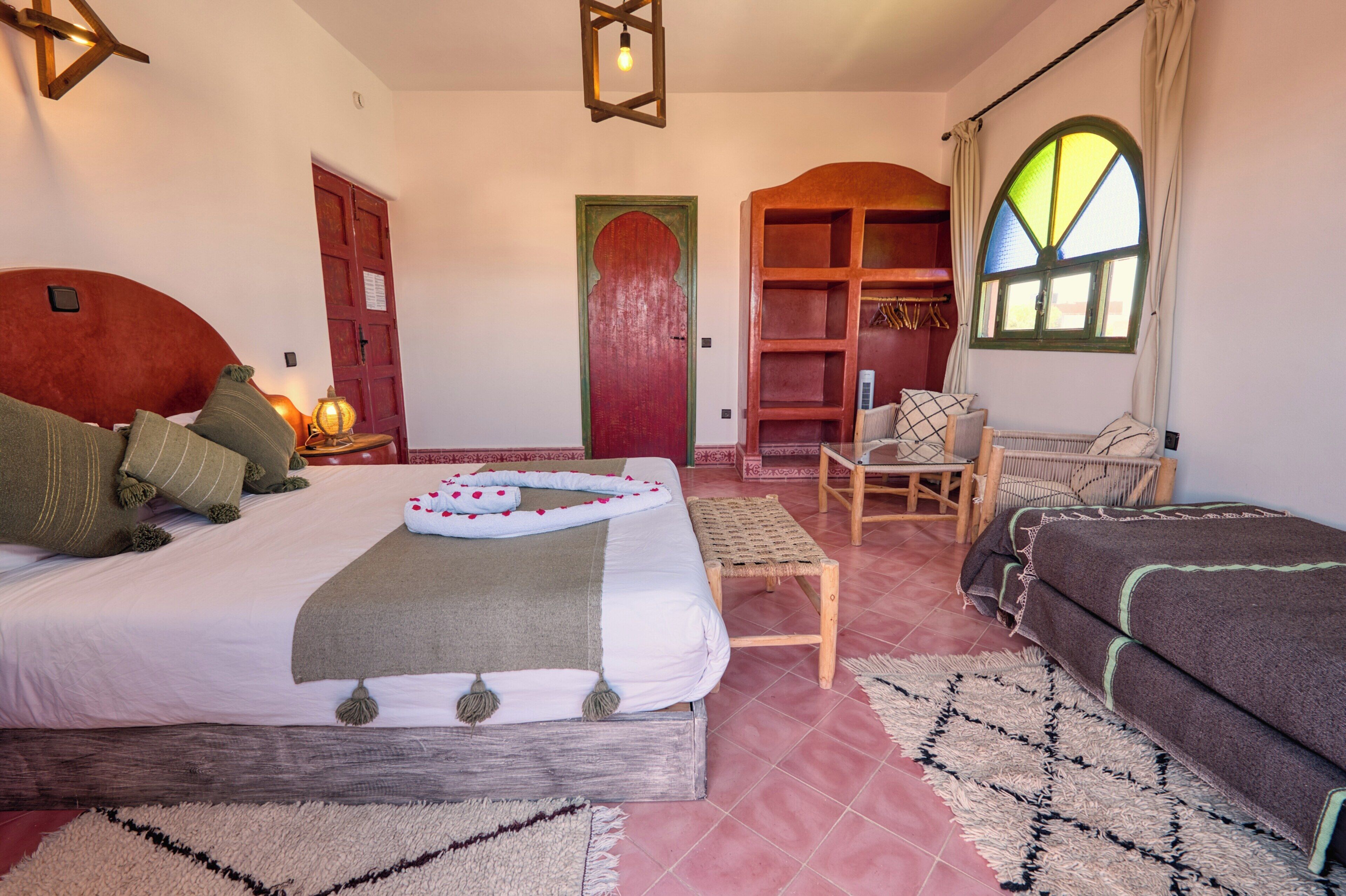 Habitación de hotel con cama, zona de estar con una silla y una mesita, armario de madera y ventana grande con cortinas.