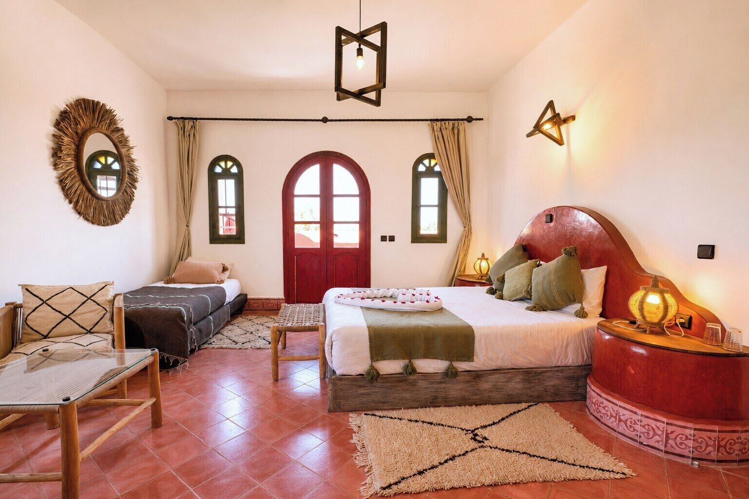 Un dormitorio con cama, dos mesitas de noche, una silla, un espejo y un ventanal con cortinas.