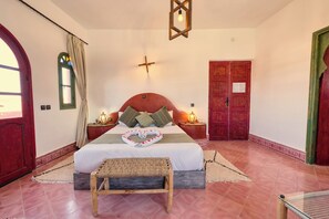 A bedroom with a bed, a wooden bench, a cross on the wall, and a door.