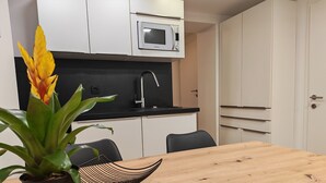 Una cocina moderna con armarios blancos, encimera negra, microondas, fregadero y una mesa de comedor con sillas.