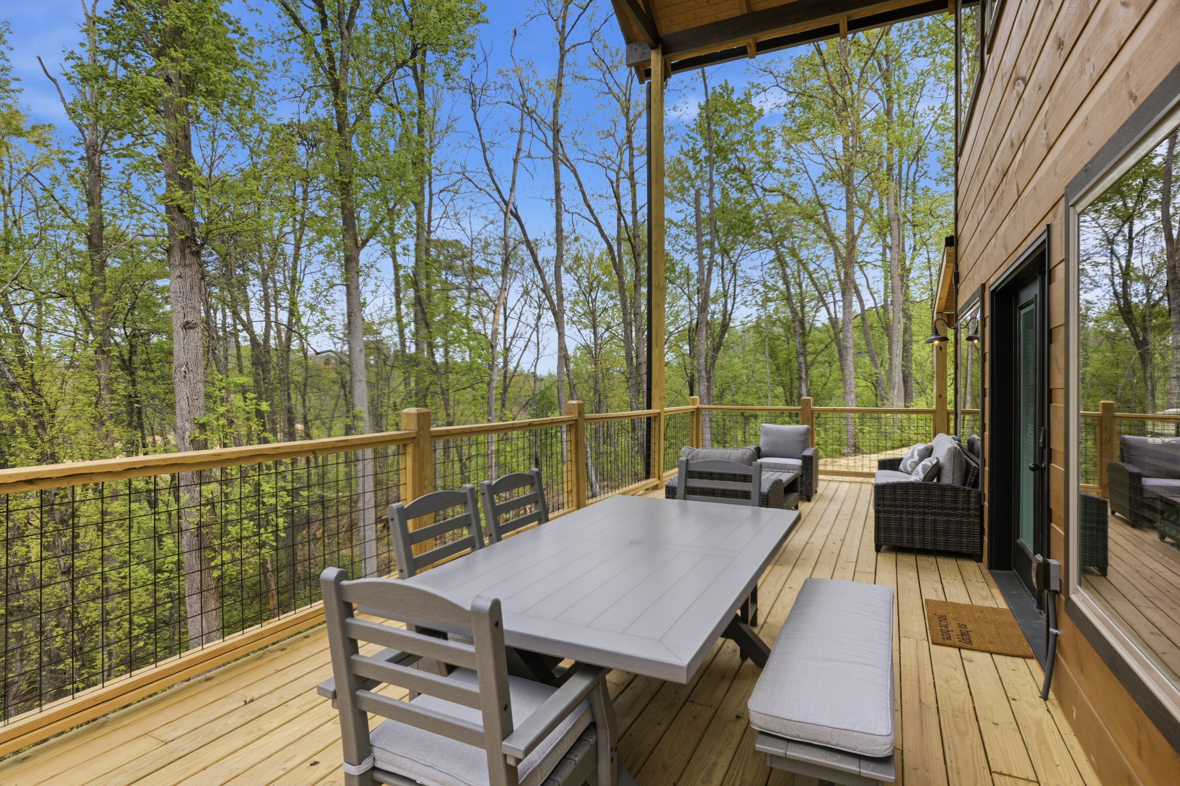 Une terrasse en bois avec une table et des chaises, un canapé et une porte vitrée donnant sur un espace intérieur.