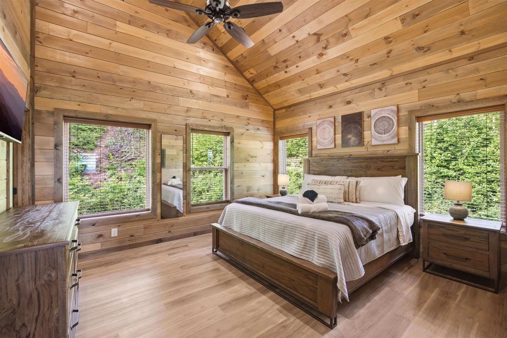 A wooden cabin bedroom with a bed, nightstands, and a ceiling fan.