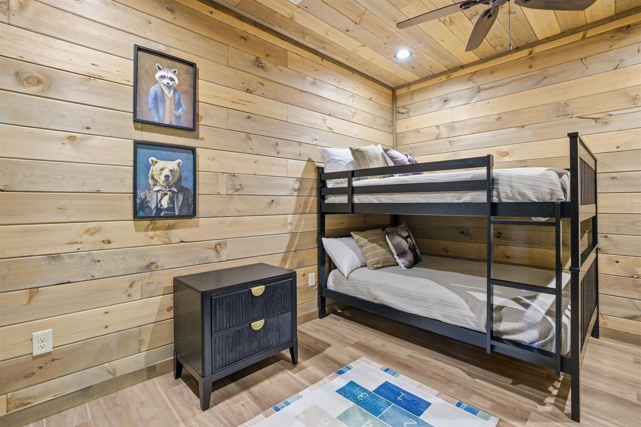 Een stapelbed met hoofdbord, een klein nachtkastje en twee ingelijste foto's aan de muur.