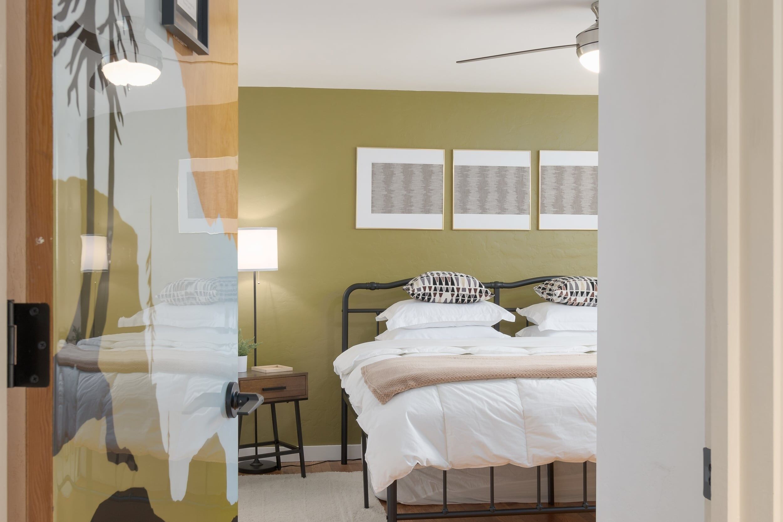 A bedroom with a bed, bedside table, lamp, and wall art.