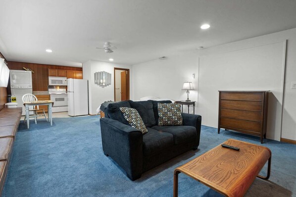 A compact living space with a kitchenette, a sofa, a wooden table, and a dresser.