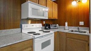 A kitchen with wooden cabinets, a white microwave, a stove, a toaster, and a sink. - Sunflower Studio - 7 Minutes To Uo & 4 Minutes To Downtown 1 Bedroom Studio (Eugene)