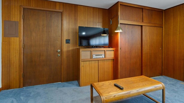 A room with a wooden wardrobe, a television on a wooden cabinet, and a small wooden table with a remote control. - Sunflower Studio - 7 Minutes To Uo & 4 Minutes To Downtown 1 Bedroom Studio (Eugene)