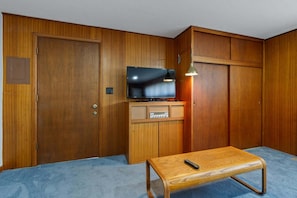 A room with a wooden wardrobe, a television on a wooden cabinet, and a small wooden table with a remote control.