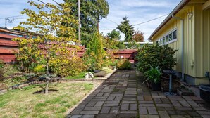 A paved backyard with a wooden fence, potted plants, and a small garden area. - Sunflower Studio - 7 Minutes To Uo & 4 Minutes To Downtown 1 Bedroom Studio (Eugene)