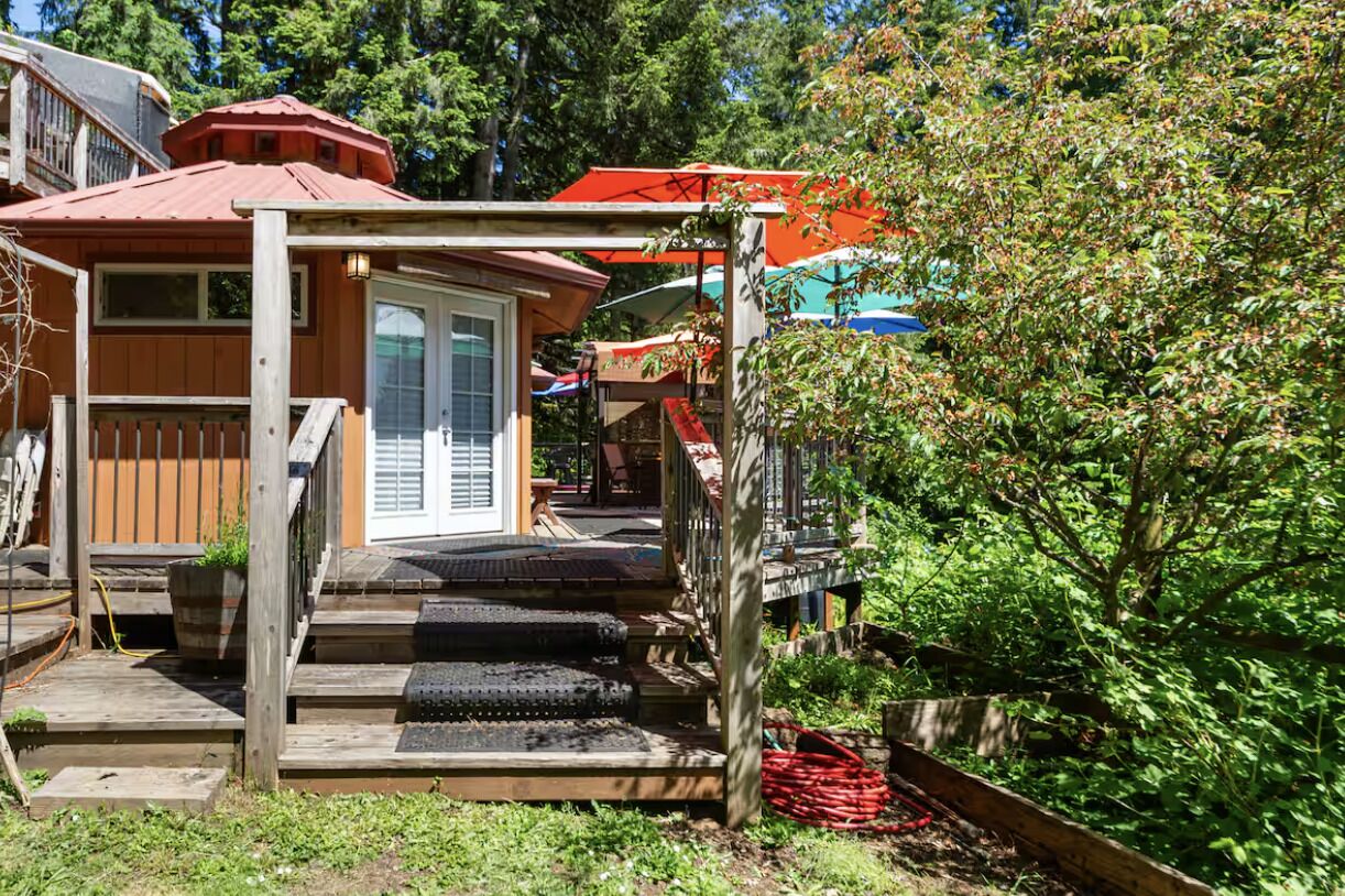 Une maison en bois avec un toit rouge, un porche avec des marches et un jardin.