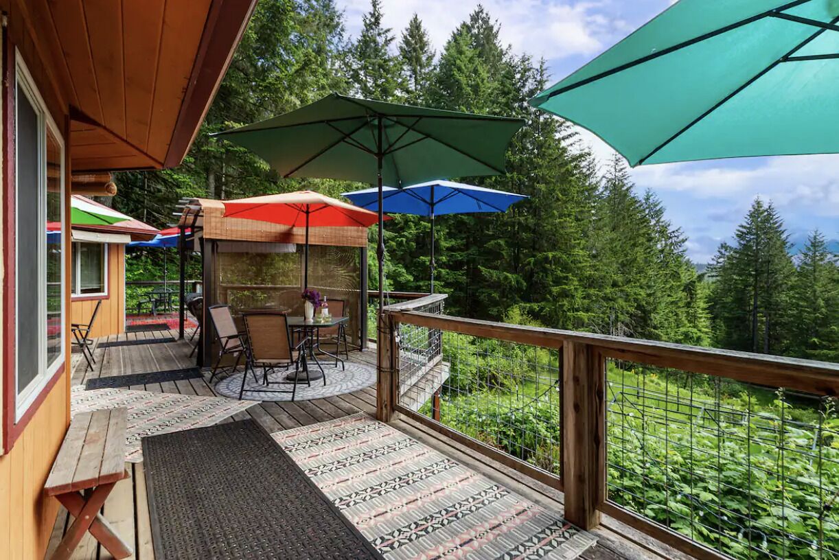 A wooden deck with outdoor furniture, umbrellas, and a view of a forest.