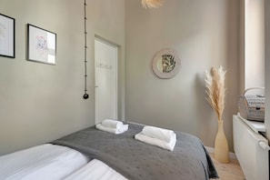 Un lit bien fait, avec deux serviettes, un miroir fixé au mur et un vase décoré de plumes d’herbe de la pampa.