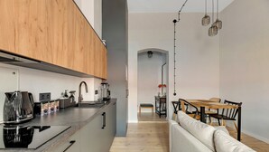 A modern kitchen with a built-in stove, wooden cabinets, and a dining area with a wooden table and chairs. - Azzuro Living Sopot - Prime Location  (Sopot)