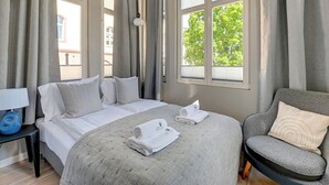 A hotel room with a bed, a chair, a lamp, and a window with curtains. - Azzuro Living Sopot - Prime Location  (Sopot)