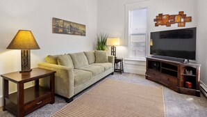 Un salon comprenant un canapé, deux tables d’appoint, une lampe, un téléviseur à écran plat, un tableau et un élément décoratif mural.