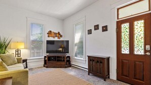 Un salon comprenant un téléviseur, un canapé, une table basse, un tapis, un meuble et une porte avec des vitraux.