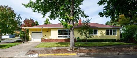 A two-story house with a garage, a tree in front, and a clear sky.