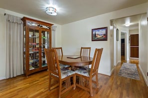 A dining area with a wooden table and chairs, a glass-fronted cabinet, and a painting on the wall. - Mellow Yellow - 7 Minutes To Uo & 4 Minutes To Downtown 3 Bedroom Home (Eugene)