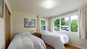 Un dormitorio con dos camas, una mesita de noche, un cuadro enmarcado y una ventana con cortinas.