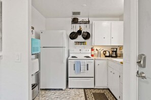 Una cocina compacta con armarios blancos, un refrigerador blanco, una estufa y un microondas.