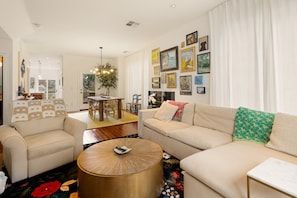 A living room with a beige sofa, a round coffee table, and a dining area with a table and chairs. - Birdhouse - Close To U Of O & Downtown 3 Bedroom Home (Eugene)