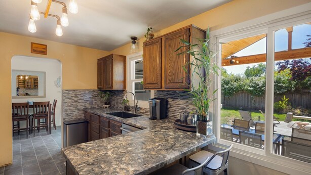 A kitchen with granite countertops, wooden cabinets, and a large window overlooking a backyard.