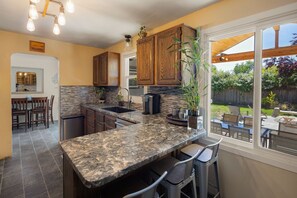 Cocina con encimeras de granito, armarios de madera y un amplio ventanal con vista a un jardín.