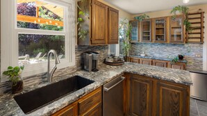 A kitchen with wooden cabinets, a granite countertop, a built-in dishwasher, and a window overlooking a garden.