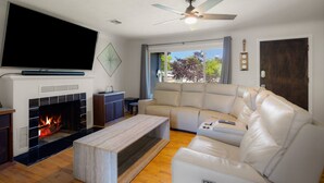 A living room with a fireplace, a large flat-screen TV, a ceiling fan, and a leather sofa.