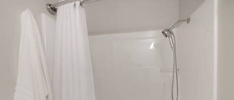 A shower with a handheld showerhead and a glass door.