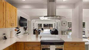 A modern kitchen with wooden cabinets, a stainless steel range hood, and a central island. - River's Rest - Waterfront Views, Hot Tub, Grill & Fire Pit 3 Bedroom Home (Walterville)
