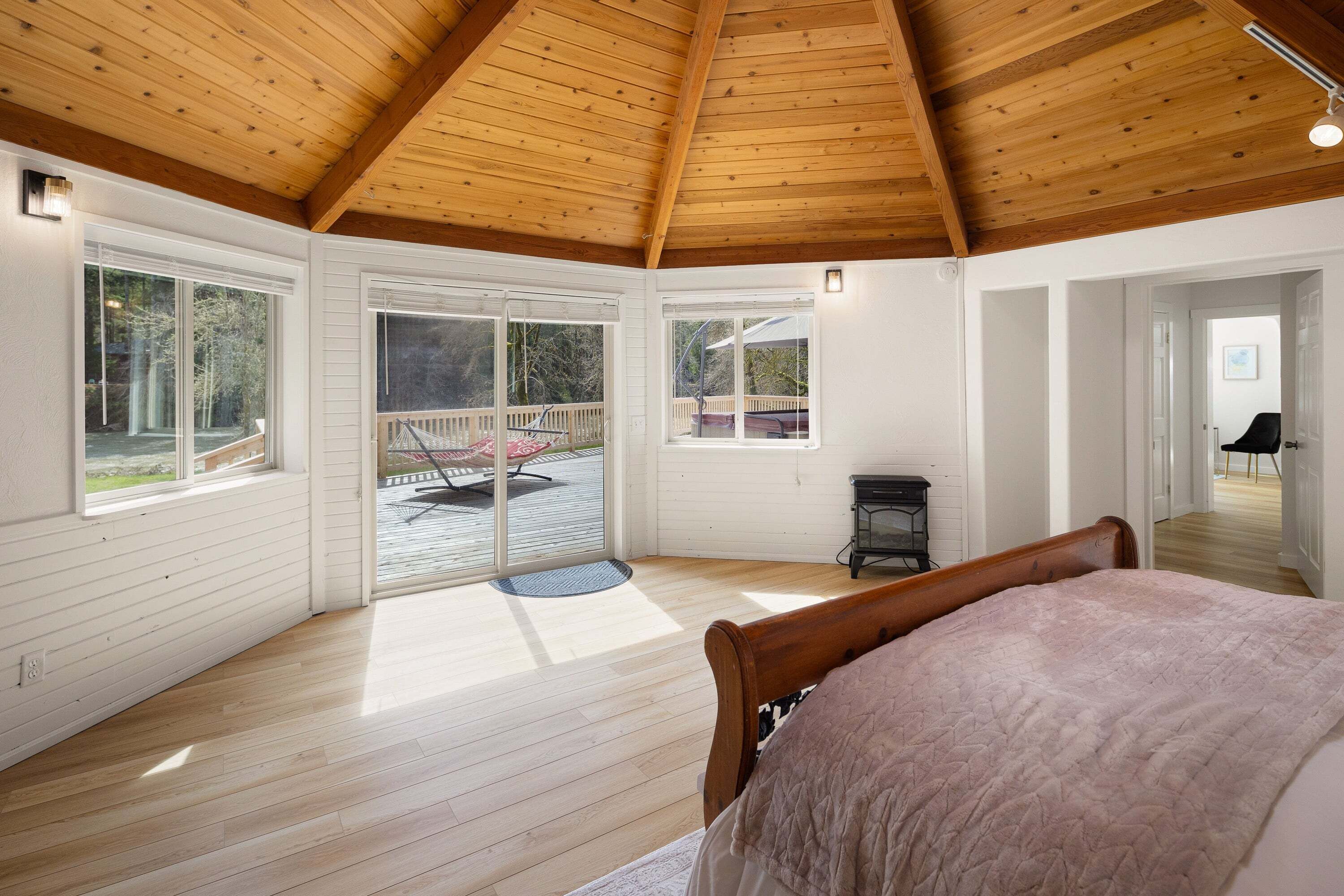 Une chambre avec un plafond en bois, de grandes fenêtres, un lit et une porte-fenêtre coulissante donnant sur un espace extérieur.