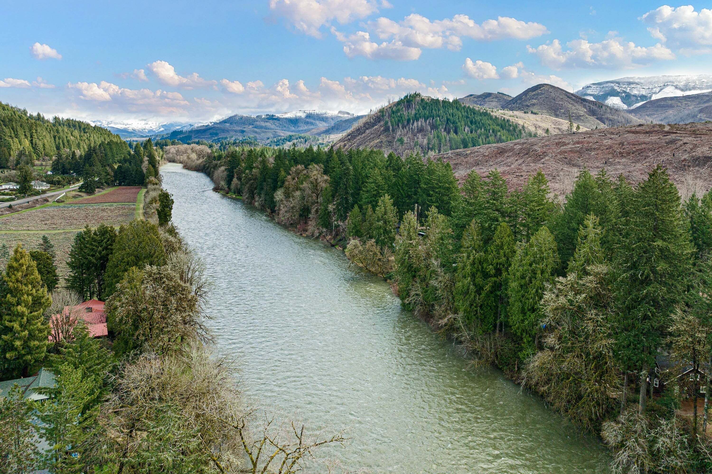 A river flowing through a valley with forested hills and a clear sky.