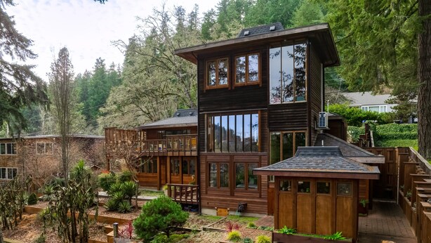 A multi-story wooden cabin with large windows, a deck, and a garden area. - Lumbermill Modern - Zen Sanctuary Near U Of O 3 Bedroom Home (Eugene)