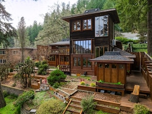 A multi-story wooden cabin with large windows, a deck, and a garden area. - Lumbermill Modern - Zen Sanctuary Near U Of O 3 Bedroom Home (Eugene)