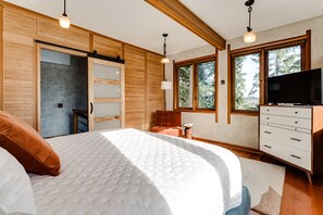 A bedroom with a bed, wooden wardrobe, TV, and a window with a view of trees. - Lumbermill Modern - Zen Sanctuary Near U Of O 3 Bedroom Home (Eugene)