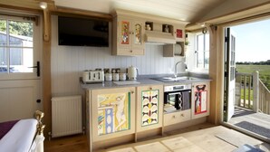Cocina compacta con horno integrado, lavamanos y televisor sobre la encimera.