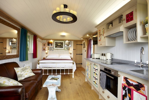 Una habitación compacta con cama, una mesita, un sofá, kitchenette y comedor.
