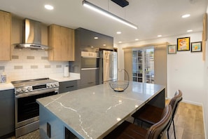 A modern kitchen with a central island, stainless steel appliances, and wooden cabinetry. - Zen Den - 10 Minutes To Autzen & Downtown 2 Bedroom Home (Eugene)