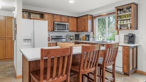 A kitchen with wooden cabinets, a white refrigerator, a microwave, a stove, and a bar area with stools. - Oakway Oasis - 6 Minutes To Autzen 4 Bedroom Home (Eugene)