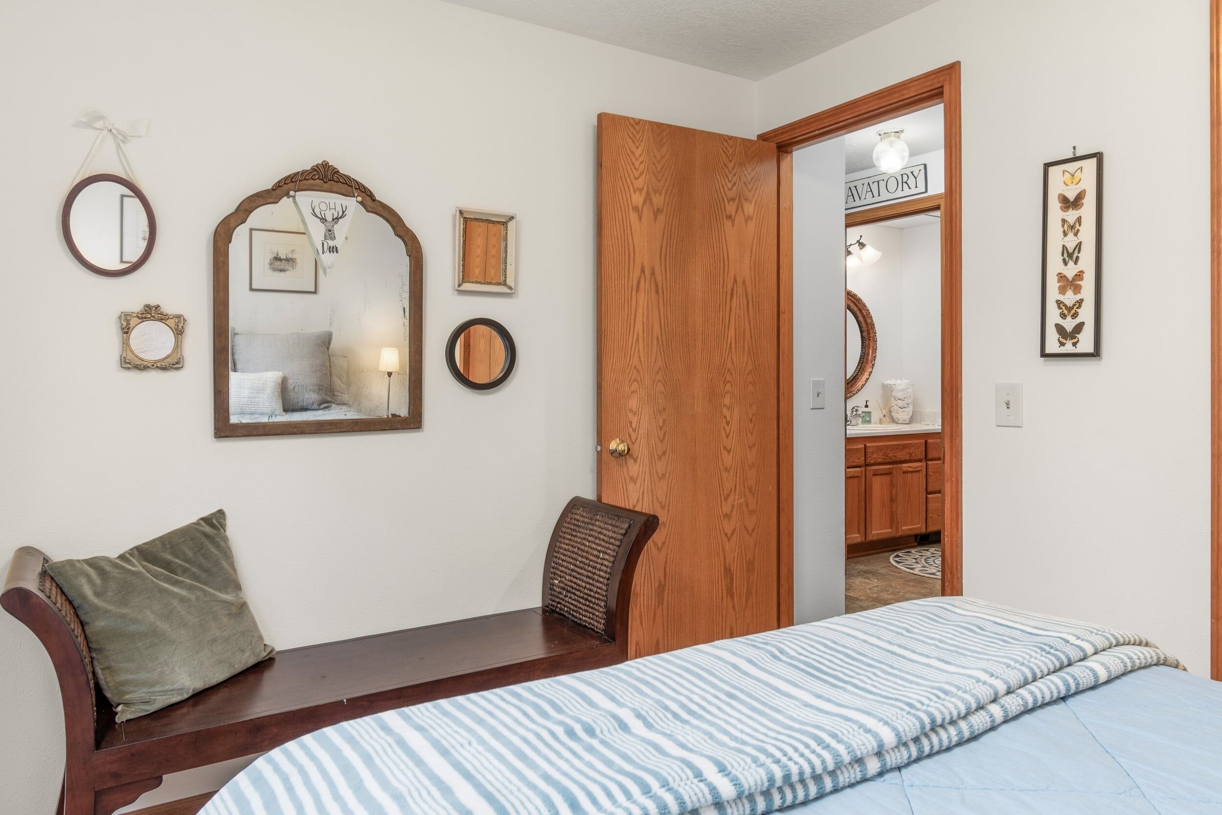 Une chambre à coucher comprenant un lit, un banc en bois, un miroir et une porte donnant sur une salle de bain.