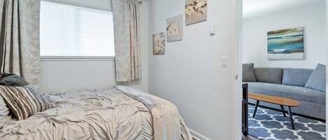 A bedroom with a bed, a window with curtains, a sofa, and artwork on the wall.