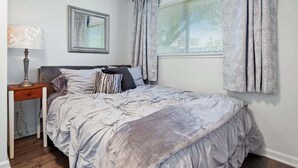 Een slaapkamer met een bed, een nachtkastje, een lamp, een spiegel en een raam met gordijnen.