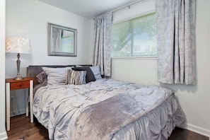 A bedroom with a bed, a nightstand, a lamp, a mirror, and a window with curtains.
