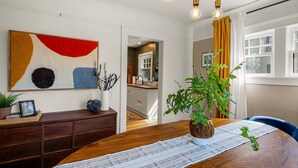 A dining area with a wooden table, a potted plant, and a painting on the wall. - Orchard Luxe - Modern Home In Walking Distance To Uo 3 Bedroom Home (Eugene)