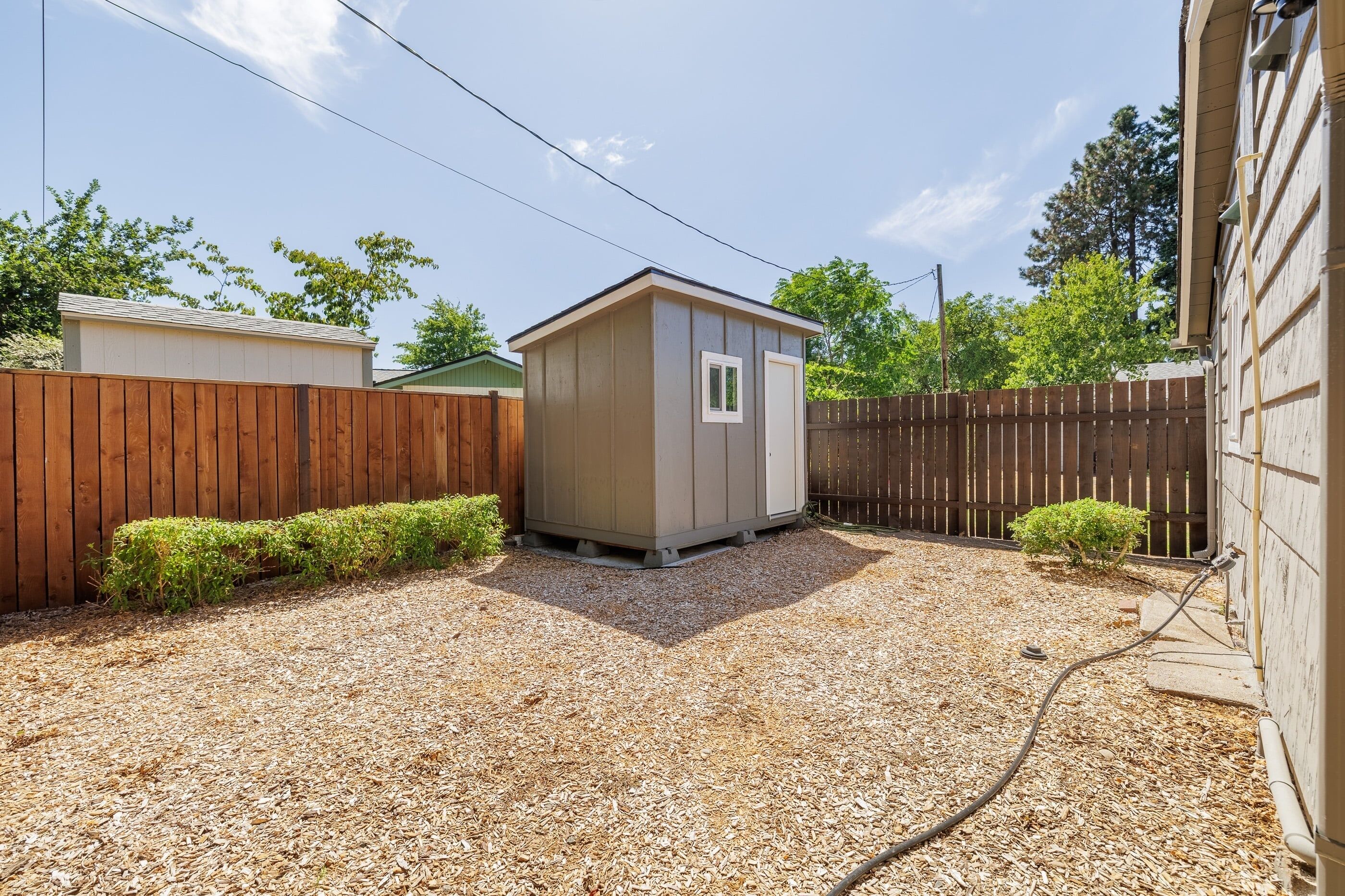 A small shed in a backyard with a wooden fence, gravel ground, and a utility line.