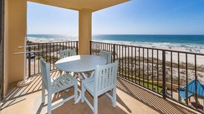 Uma varanda com mesa e cadeiras, com vista para uma praia e oceano.