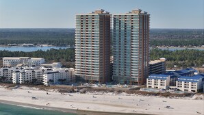A high-rise hotel with multiple balconies, a beach, and a forested area in the background. - Phoenix Gulf Towers 1005 4 Bedroom Condo (Orange Beach)